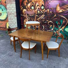 a wooden table and four chairs in front of a wall with graffiti painted on it