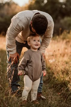 a man bending over to kiss a toddler's face in a field with tall grass