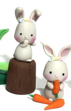 two small figurines sitting on top of a wooden stump with carrots in front of them