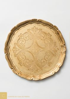 a gold plate with ornate designs on it sitting on a white table top next to a ruler