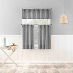 a kitchen with white walls and gray curtains on the windowsills, along with a table in front of it