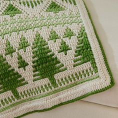 a green and white crocheted blanket with trees on it