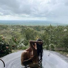 a naked woman sitting in the middle of a pool with trees and bushes behind her