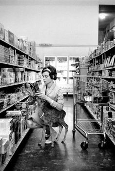 a woman kneeling down next to a dog in a store aisle while reading a book