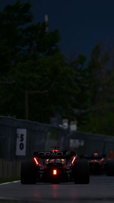 a race car driving on a track at night time with the lights on and trees in the background