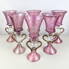 five pink glass vases sitting next to each other on a white counter top with pearls