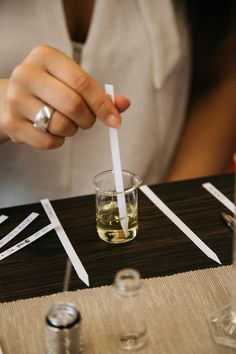 a woman is holding a straw in her hand while sitting at a table with glasses and knives on it