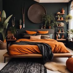 a bed with orange sheets and pillows in a room filled with potted plants on the wall