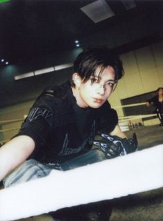 a young man sitting on top of a skateboard in an indoor area with other people