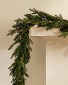 a christmas garland with lights hanging from it's sides on a mantle in front of a white wall