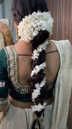 a woman with flowers in her hair is wearing a white sari and braids