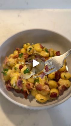 a bowl filled with potatoes and bacon on top of a white counter next to a spoon