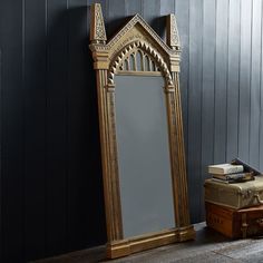 an ornate wooden mirror sitting next to a suitcase on the floor in front of a black wall