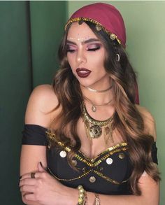 a woman with long hair wearing gold jewelry and a red headdress is posing in front of a green wall