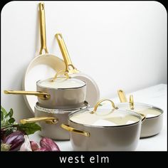 three pots and two pans with gold handles on the side, sitting next to each other