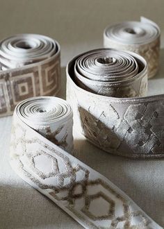 three rolls of white and silver decorative ribbon on a gray surface with an intricate design