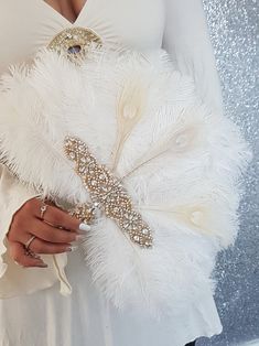 a woman wearing a white dress holding a feathered cross brooch