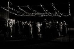 a group of people standing around each other in the dark with string lights on them