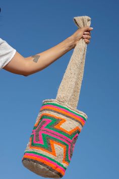 a woman holding a multicolored bag in the air with blue sky behind her