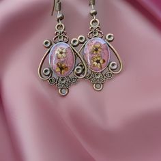 Victorian-inspired earrings, featuring genuine light pink dried flowers sourced from Armenia. These handcrafted antique aesthetic earrings are designed to infuse your look with a touch of timeless elegance and a dash of romance. Each pair of earrings is a unique work of art, carefully crafted to capture the essence of vintage charm. The delicate, preserved pink flowers add a touch of nature's beauty to your accessory collection, making them a perfect choice for nature lovers and those who apprec Pink Bohemian Jewelry With Pressed Flowers, Bohemian Pink Jewelry With Pressed Flowers, Rose Gold Pressed Flower Earrings, Pink Flower Metal Earrings, Pink Flower-shaped Metal Earrings, Vintage Handmade Pink Flower Earrings, Pink Dangle Jewelry With Pressed Flowers, Handmade Vintage Pink Flower Earrings, Pink Handmade Vintage Flower Earrings