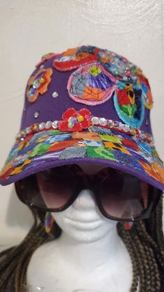 You can still look cute on a bad hair day with this product.  This hat is so colorful and cheerful and has earrings to match. It's designed with bright, colorful fabric made into a jumbo fabric flower with mini accent flowers on a purple background. The bright colors give 90s vibes. The bill is also decorated with colorful fabric squares and accented with faux gemstones. Hat size is adjustable. Cheap Multicolor Mini Hats, Purple Cap As A Gift, Purple Hats As Gifts, Purple Hat As A Gift, Playful Purple Adjustable Hat, Purple Hat For Spring As A Gift, Purple Hat For Spring Gift, Purple Hat As A Spring Gift, Purple Spring Gift Hats