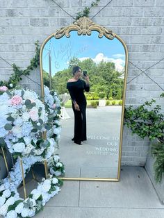 a woman taking a selfie in front of a large mirror with flowers on it