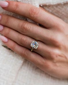 a woman's hand with a diamond ring on her left hand, wearing a white sweater