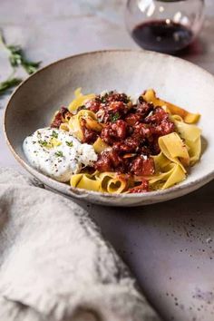 a white bowl filled with pasta and sauce on top of a table next to a glass of wine