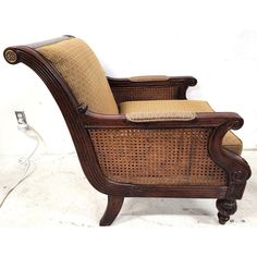 an old wooden chair with wicker back and arm rests against a white wall next to a plugged in charger