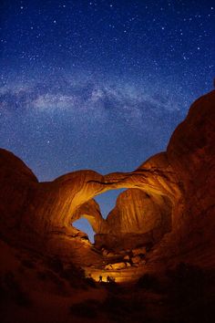 the night sky is filled with stars and light up rock formations, as well as people walking through them