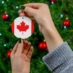 someone holding up a christmas ornament with the canadian flag on it in front of a christmas tree