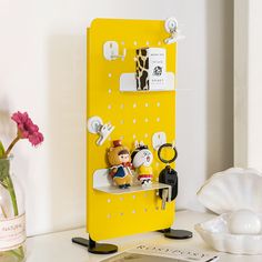 a yellow refrigerator with magnets attached to it on a table next to a flower vase