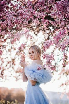 a woman in a blue dress standing under a tree with pink flowers