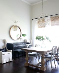 a dining room table with chairs and a piano in front of the window, next to a couch