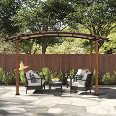 two chairs and a table under a pergolated gazebo with trees in the background