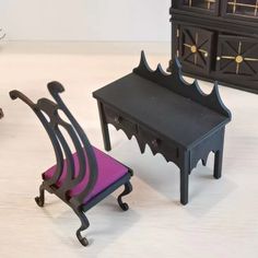 two miniature chairs and a small table with a purple cushion sit on a white surface