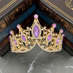 Regina's tiara is a magnificent piece of art for your head. Large lavender purple marquise shaped crystals dominate with small clear round crystal detailing all set into gold colored metal.  Max Height at Center: 3.25 Inches  Total Length End to End: 12.25 Inches  Length of Embellishment: 11 Inches Head Opening: 6.75 Inches Tiara is adjustable by carefully bending and stretching the ends apart to fit most hair styles and head sizes.  Tiara features loops on each end to secure to hair with bobby pins. Item ships from Michigan, USA. WARNING: CHOKING HAZARD This is not a toy.  This item is not intended for use by children under the age of 5 years old.  There are small pieces that could fall off and create a choking hazard.  All use of this product by any minor, child or dependent should be su Teardrop Crown Jewelry With Rhinestones For Wedding, Elegant Crystal Crown Headpiece, Gold Crystal Crown Jewelry, Gold Crystal Crown Shaped Jewelry, Gold Crown Design Headpiece With Pinched Crown, Princess Style Gold Jewelry For Party, Gold Regal Headpiece With Tall Crown, Gold Jeweled Crown Jewelry, Regal Gold Crown For Wedding