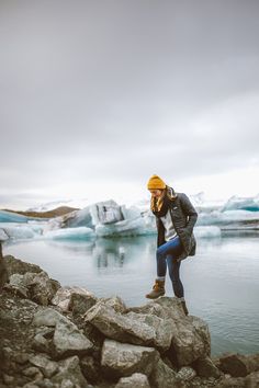 a woman is standing on rocks by the water with icebergs in the background