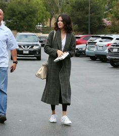 a woman is walking in the parking lot with another man behind her looking at something