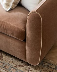 a brown couch sitting on top of a wooden floor next to a rug and pillows