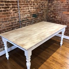 a white table sitting on top of a hard wood floor next to a brick wall