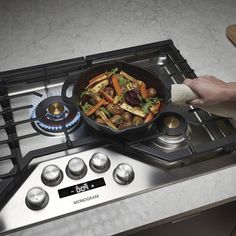 a person is holding a pan with food on top of the burners in front of an oven