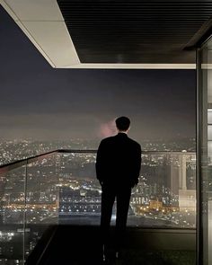 a man standing in front of a window looking out at the city lights and skyscrapers