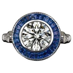 Art Deco style ring features a lively and substantial 1.80ct diamond surrounded by a glamorous ring of royal blue natural sapphires. Certified by GIA with Excellent grades in all finishing categories, the diamond has fantastic brilliance! In a classic target ring design, the diamond is encircled by a rich blue border of sapphires. The effect is an air of chic Art Deco sophistication! It is an excellent choice for an elegant and historied engagement or right hand ring! Excellent Grades, Target Ring, Sapphire Halo Ring, Vintage Cocktail Ring, Chic Art, Right Hand Rings, Estilo Art Deco, Fine Jewels, Halo Ring