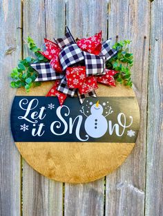 a wooden sign that says let it snow on the side of a fence with a bow