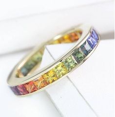 two rings with different colored stones on them sitting on top of a white surface,