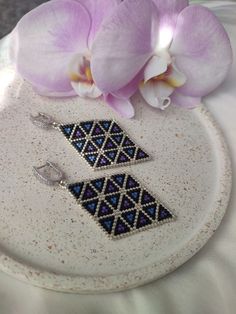 a pair of earrings sitting on top of a white plate next to a purple flower