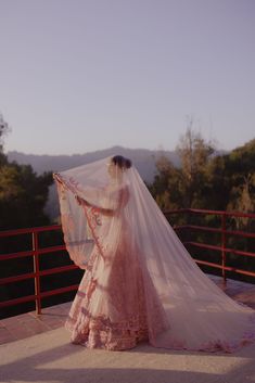 a woman in a wedding dress with a veil on her head looking at the mountains