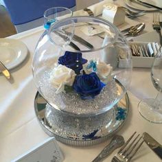 the table is set with silverware and blue flowers in a glass bowl on top of it