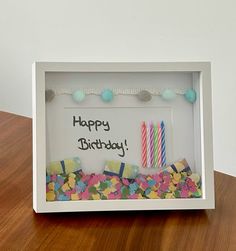 a birthday card in a white box with confetti and candles on the table